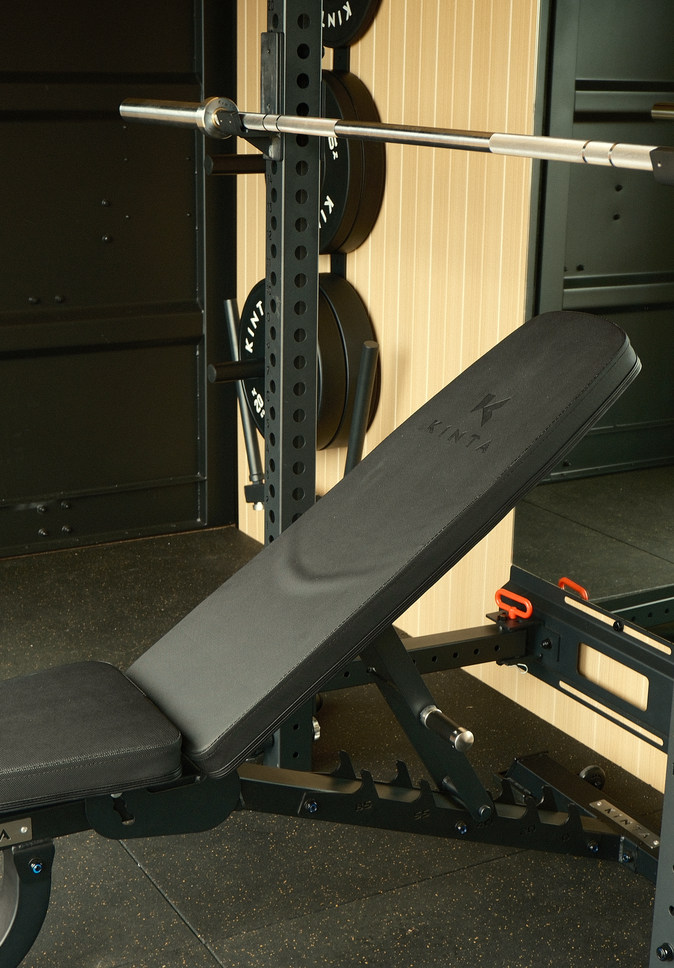 Adjustable bench set up in the rack, barbell and plates behind