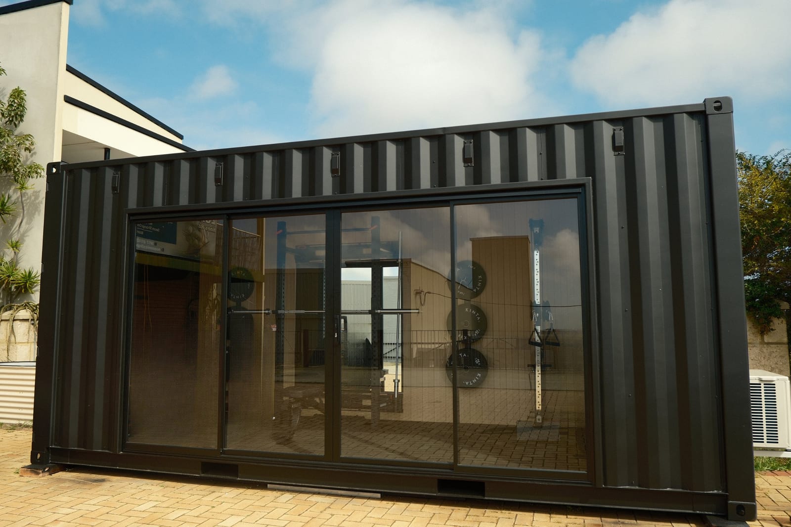 A crgo container gym on brick paving, glazed sliding doors along its front