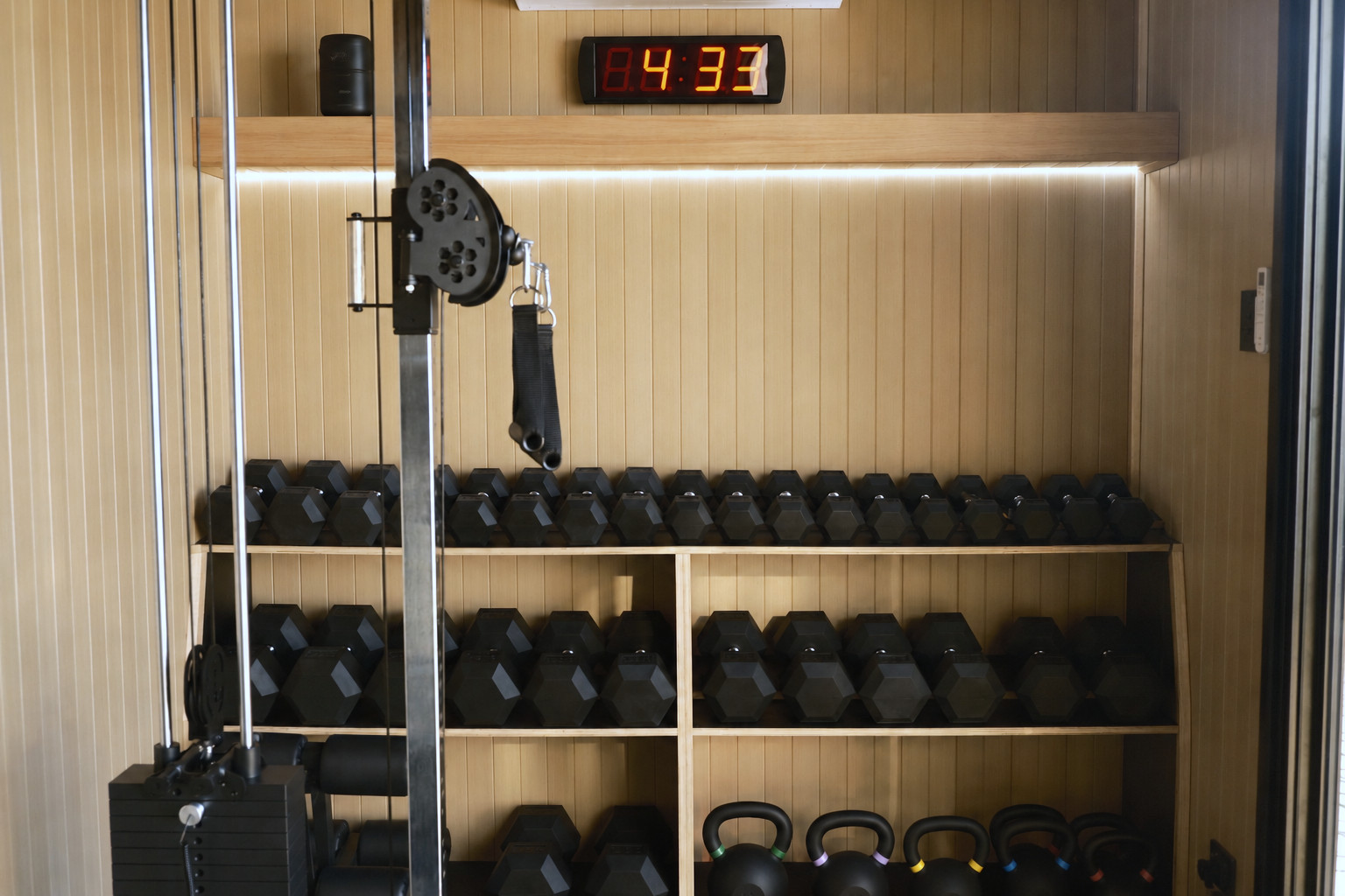 Storage wall of a crgo unit: interval clock, dumbbell rack, kettlebells and cable stack